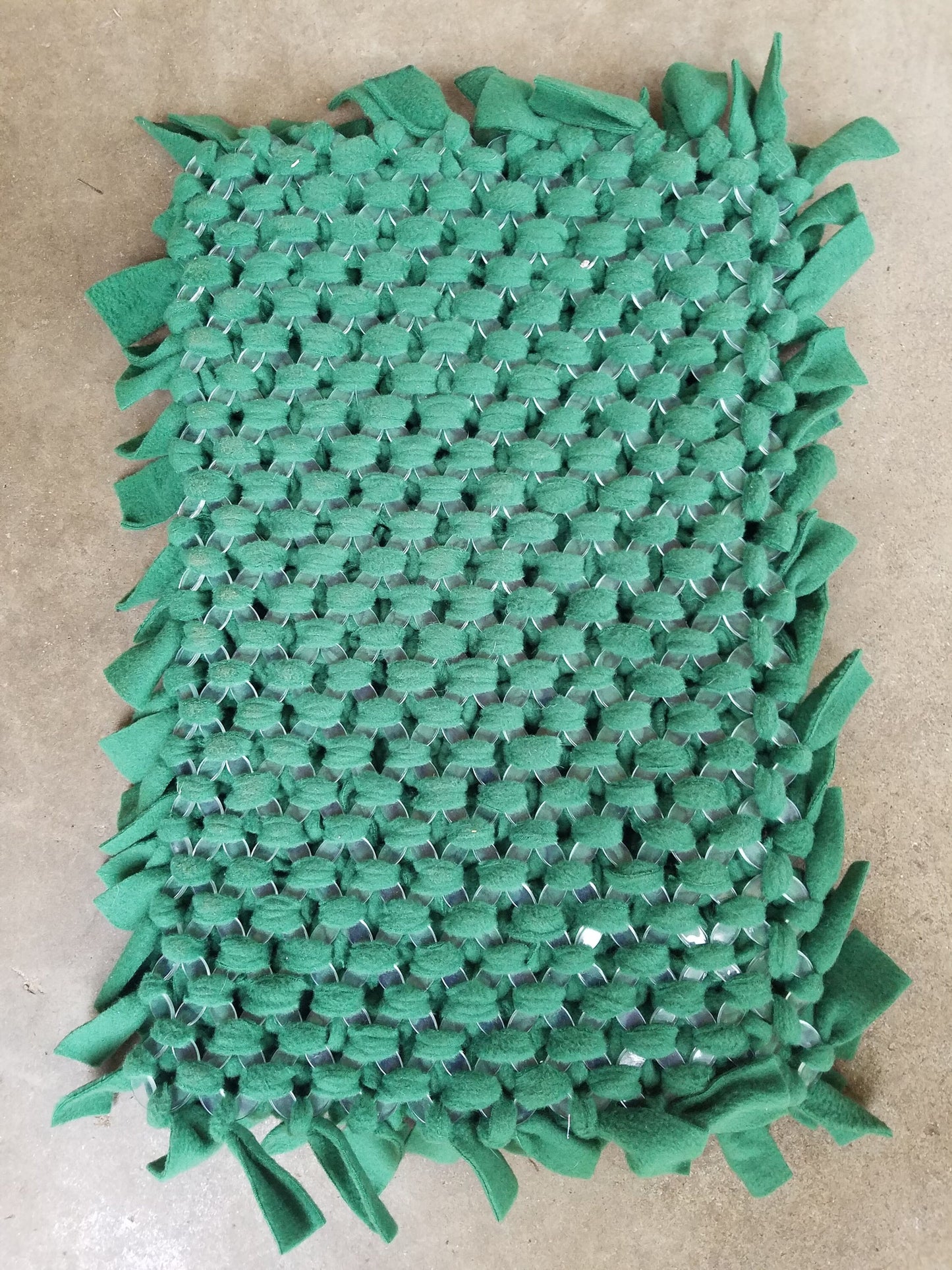 a green, woven fabric with a textured, woven appearance. The fabric has a slightly crinkled texture and appears to be made of a material that resembles cotton or a similar natural fiber. The fabric is displayed on a flat surface, possibly a table or a countertop.