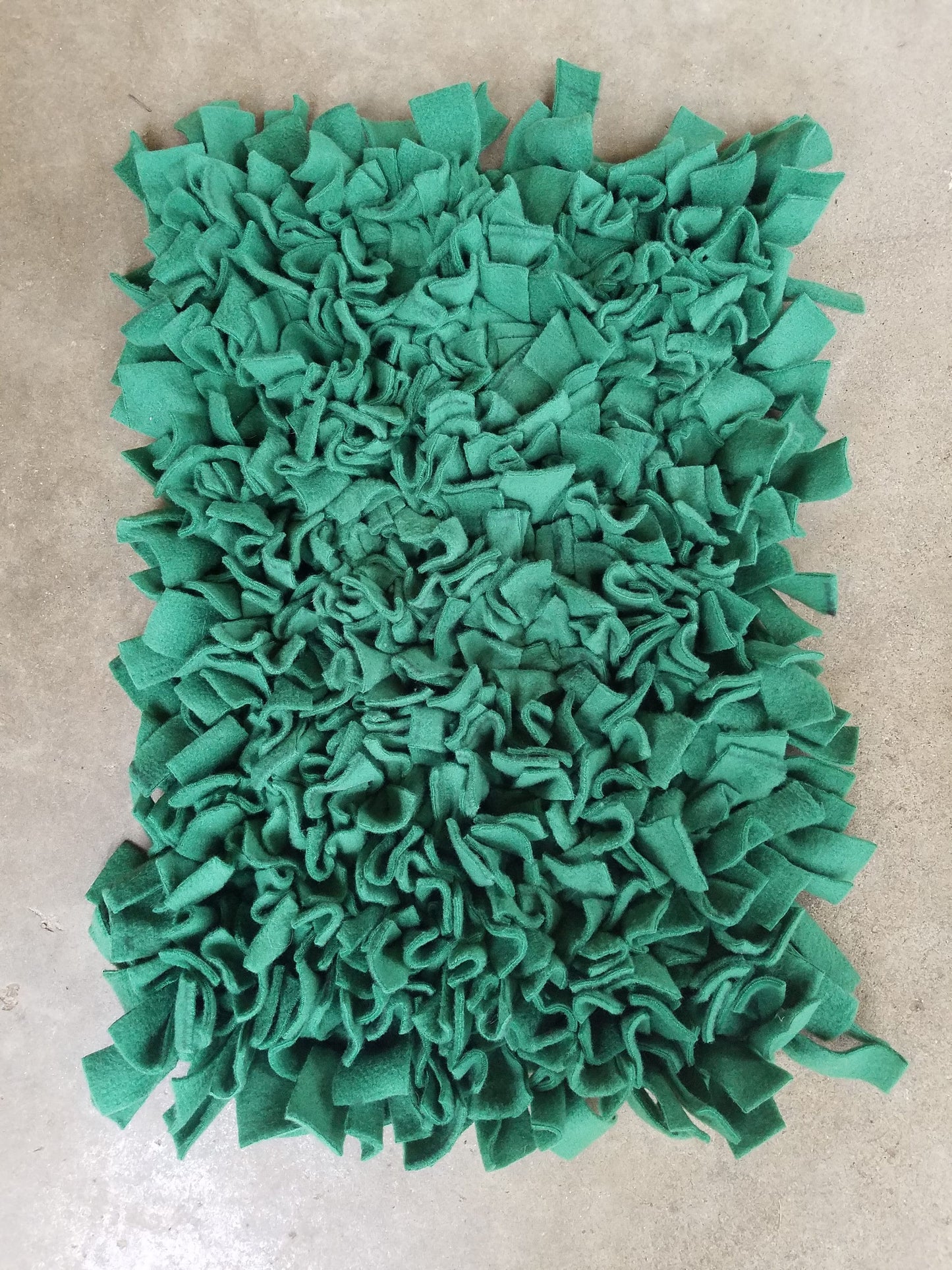 a large, green, fluffy material resembling a plush or a decorative textile. It appears to be a textile made from small, square-shaped pieces of fabric or material, creating a textured and visually interesting surface.