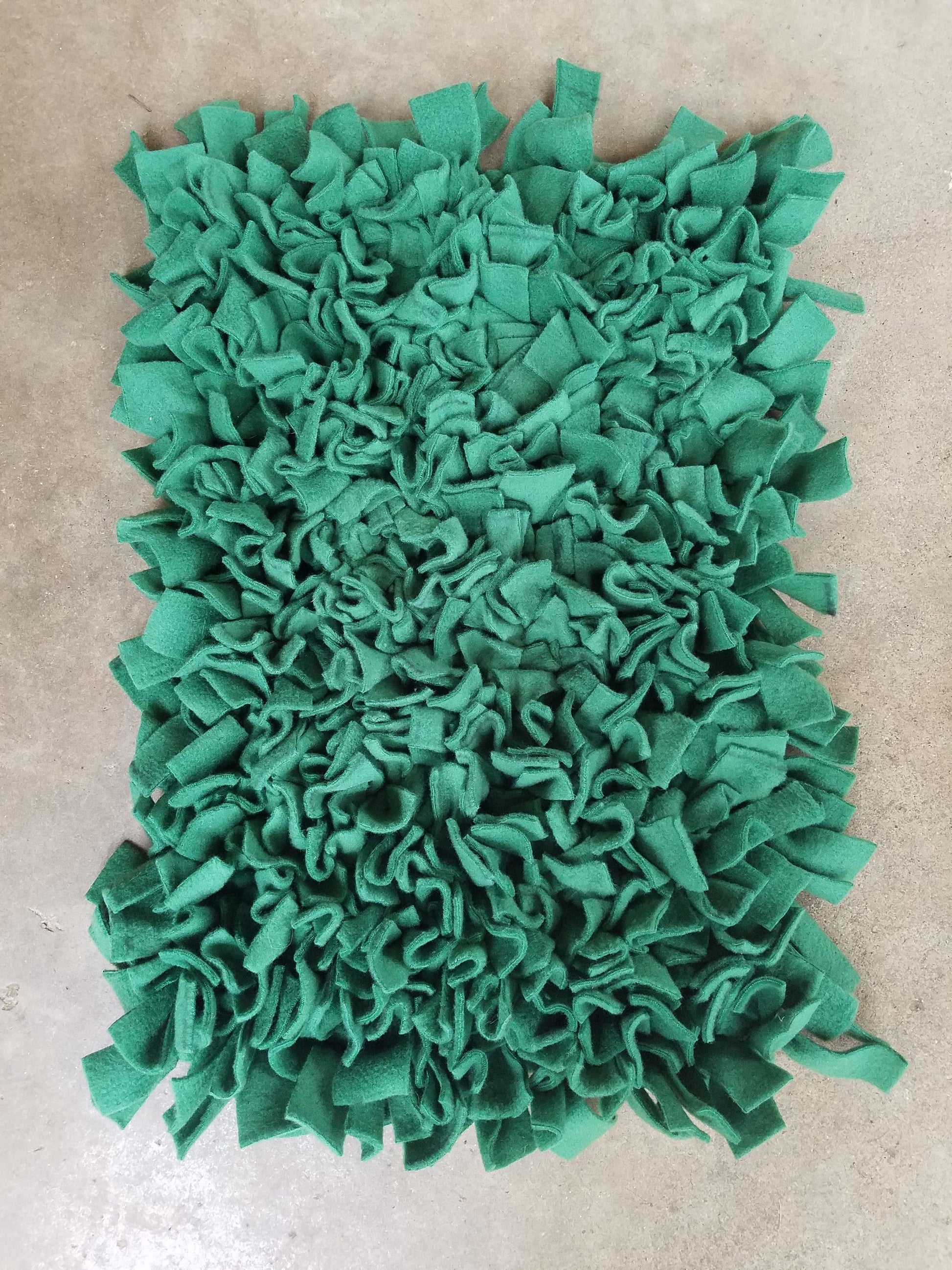 a large, green, fluffy material resembling a plush or a decorative textile. It appears to be a textile made from small, square-shaped pieces of fabric or material, creating a textured and visually interesting surface.